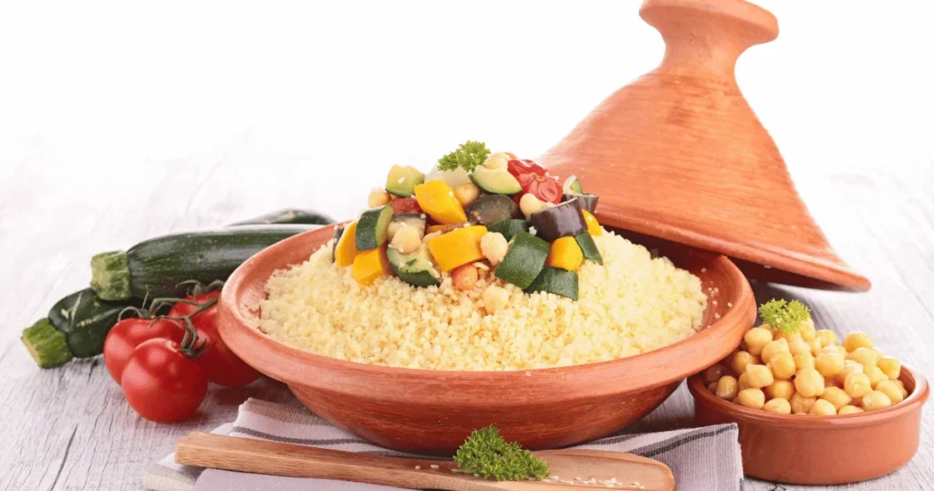 A plate of couscous with chicken, zucchini, red bell pepper, carrots, and cherry tomatoes, garnished with fresh parsley.